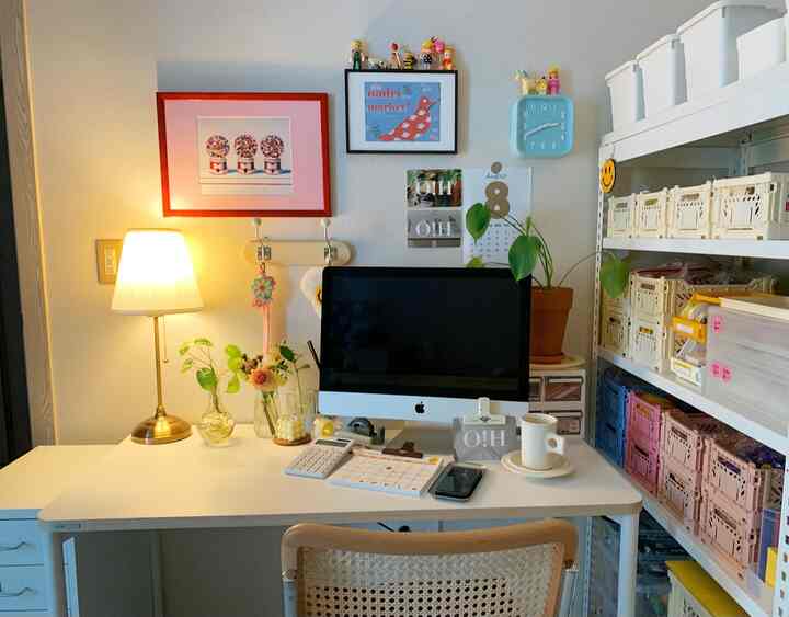 Bright white and wood-toned home office featuring an iMac on desk with desk lamp, and organized storage boxes on right shelving, neat workspace