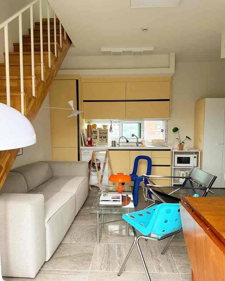 黄色調のキッチンとモダンなソファ、多彩なチェアが配置された居心地の良いロフトリビング