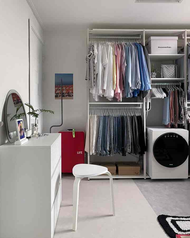 White and blue toned walk-in closet with hanging wardrobes, compact dryer, vanity, and stool in a tidy space