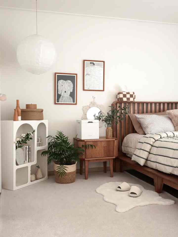 明るい白い壁面にナチュラルな木目調のベッドとナイトテーブル、植物が配置された落ち着いた寝室のインテリア