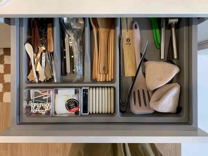 グレー調のハンセム製キッチン下部キャビネットの引き出し内、整然と並べられたカトラリーと調理器具がある雰囲気のある収納スペース