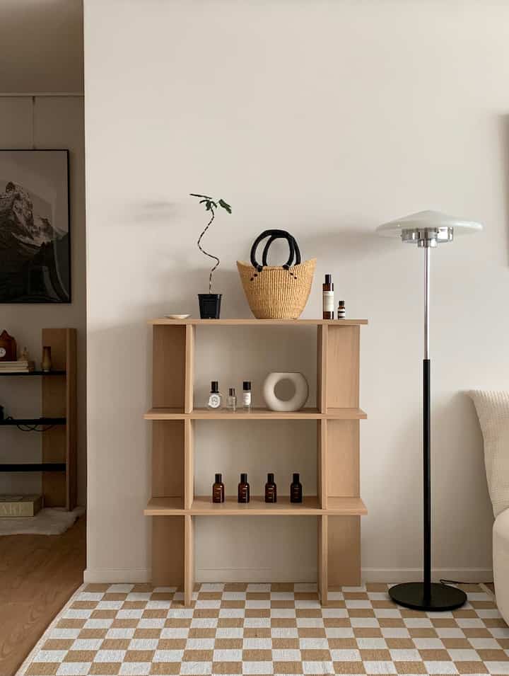 明るい木目調と白い壁のリビング、シンプルな棚とフロアランプ、整然としたオブジェが配置されたミニマルで自然な空間