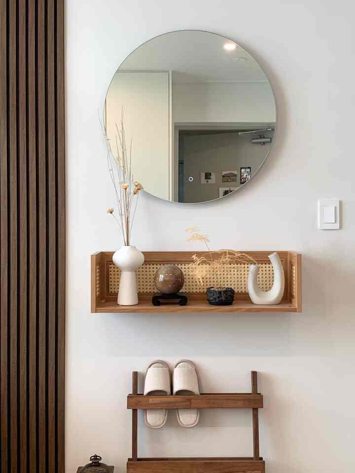 白い壁と木目調の棚に小さなオブジェと回転する球体が配置されたシンプルな玄関空間