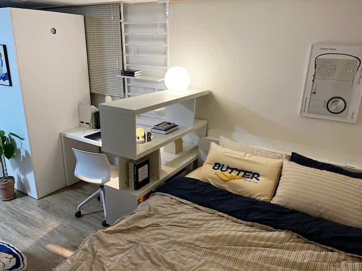 A white and natural tone bedroom featuring a low-frame room divider and a home office desk, creating a clean and organized space