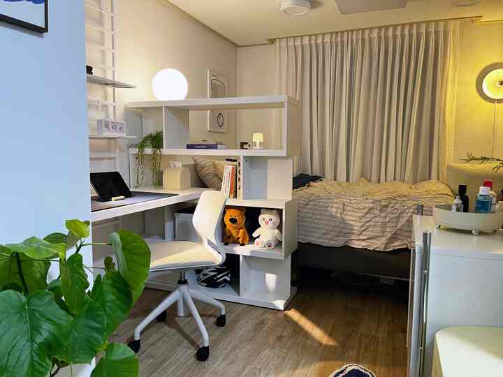 Compact bedroom and home office space in white and wood tones, featuring a desk, bed, and cozy atmosphere