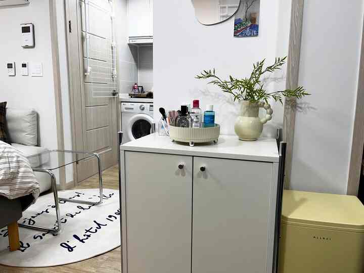 Bright white and beige toned compact living room featuring a low white cabinet, round mirror, and odor-proof trash bin with a clean open feel