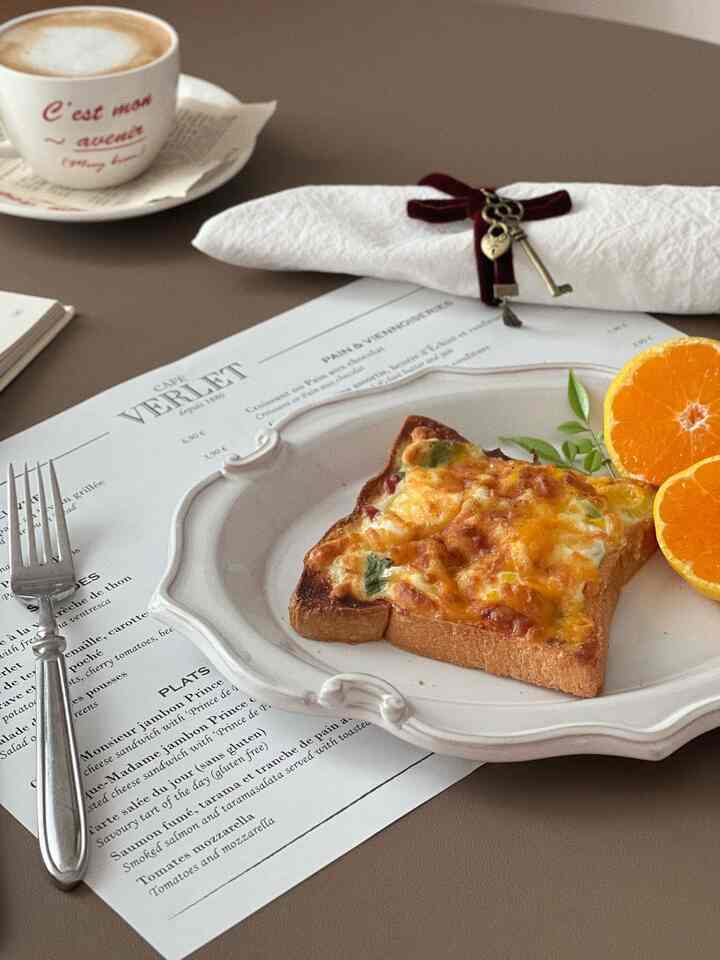 Cozy home cafe brunch featuring white plate with cheesy toast and orange slices on warm brown table surface