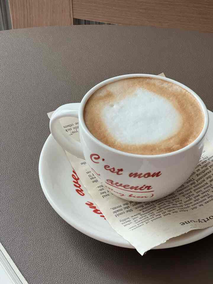 ブラウンの木目調の円形テーブルの上にヴィンテージの英字ペーパーとコーヒーカップが配置された雰囲気のあるおうちカフェ風インテリア