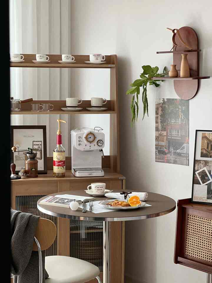 ナチュラルな色調とブラウンが調和するダイニングルーム、円形テーブルとコーヒーマシン、木製棚が配置された温かみのあるおうちカフェ空間