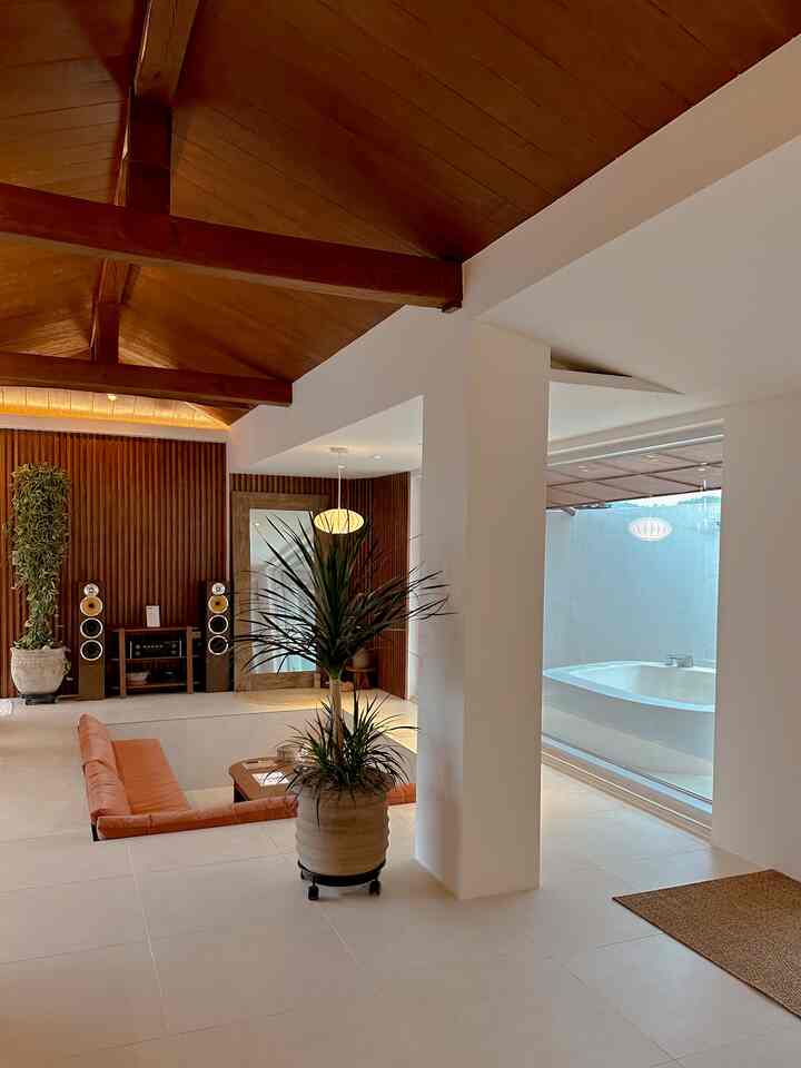 Warm wood-toned ceiling and beige tiled floor, with an orange sofa and large plants in an open living room space