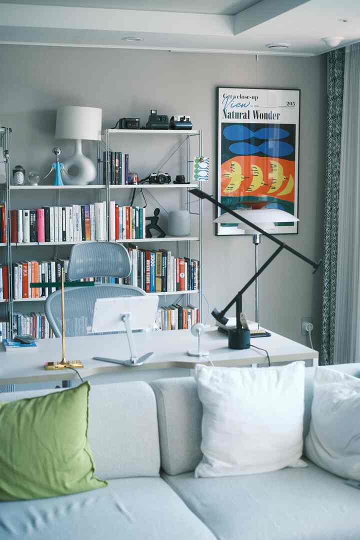 White and gray toned living room study featuring a desk with Aeron chair and large bookshelf in a modern setup