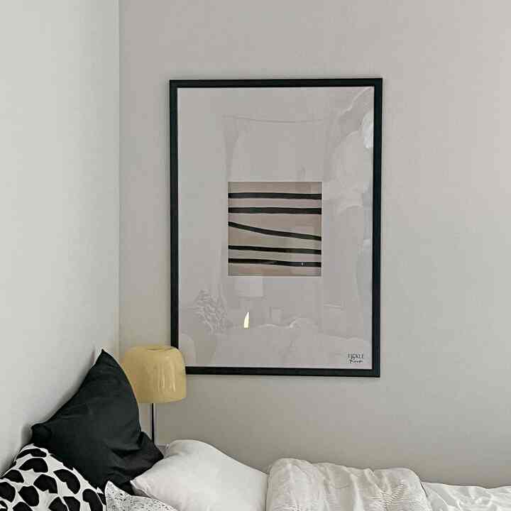 白と黒のトーンの寝室、シンプルな黒い額縁とストライプのポスターが中央の壁に配置された落ち着いた雰囲気のインテリア