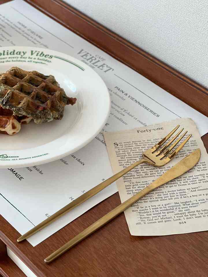 ゴールドのカトラリーが置かれた木目調のテーブルにレタリングの皿とワッフルがあるおうちカフェ風の空間