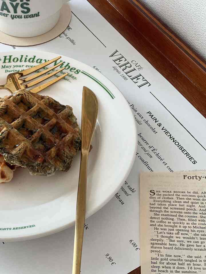 Home cafe style setup featuring white table paper with vintage English lettering, gold cutlery, plate, and mug placed on top