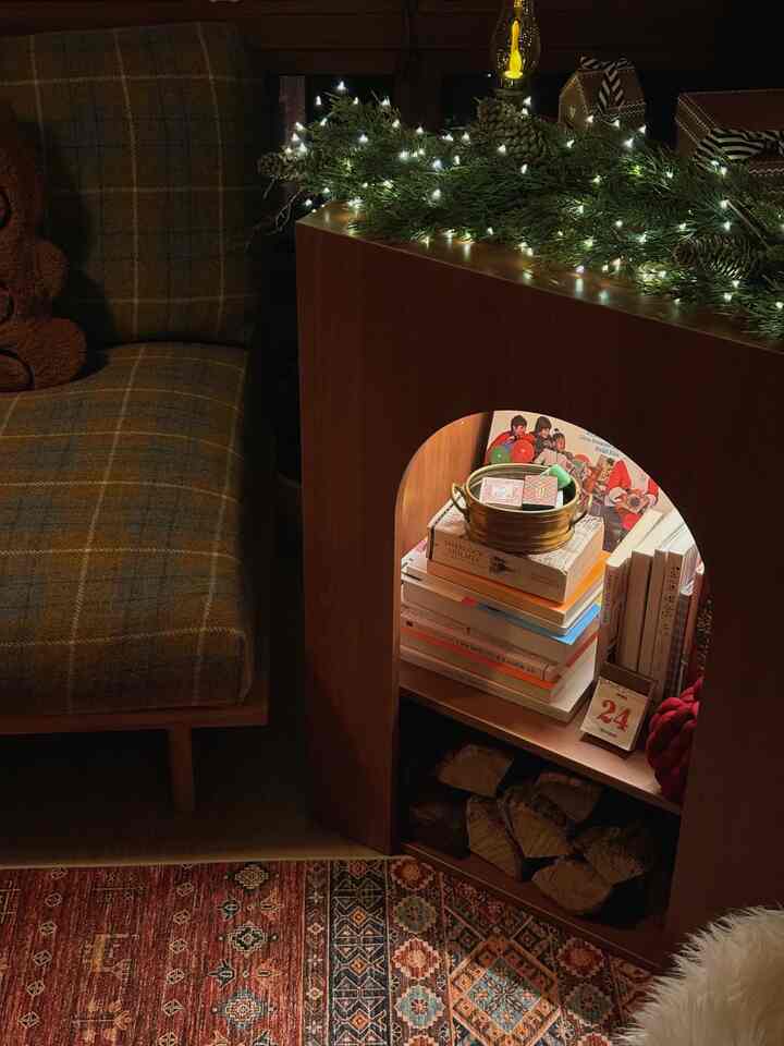暖かみのあるウッドトーンとヴィンテージスタイルのクリスマスリースが置かれた壁暖炉コンソールとチェック柄ソファが配置された居心地の良いリビングルーム