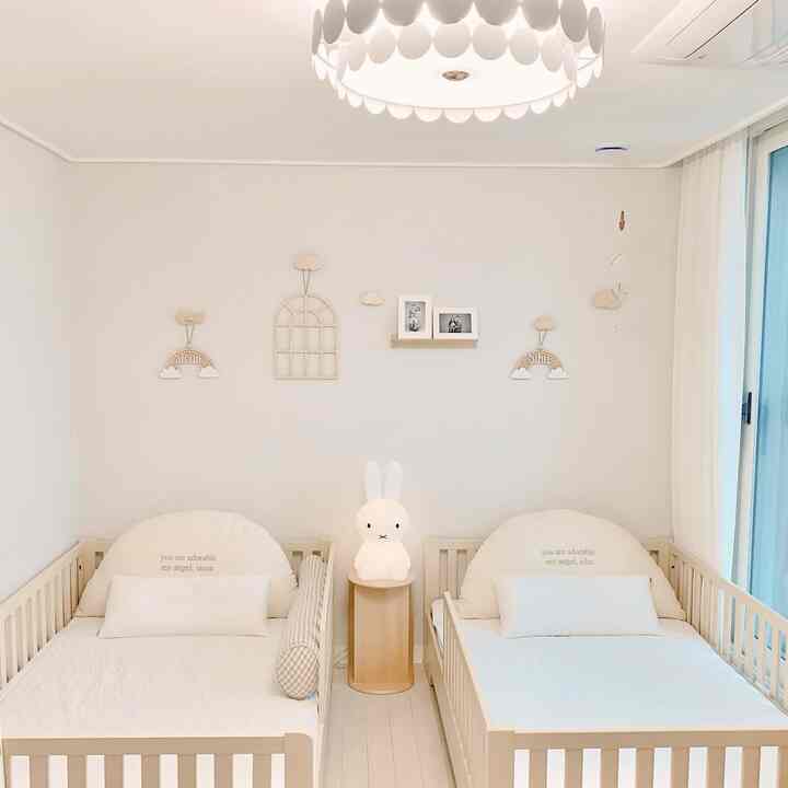 白と木目調の子供部屋、シンプルでナチュラルな雰囲気の中にベビーベッドが2つとムードランプが配置された印象的な空間