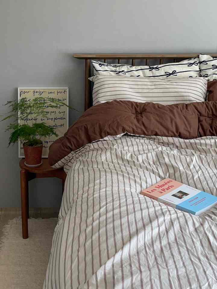 Calm gray walls and brown striped bedding in a bedroom with a wooden headboard creating a cozy atmosphere