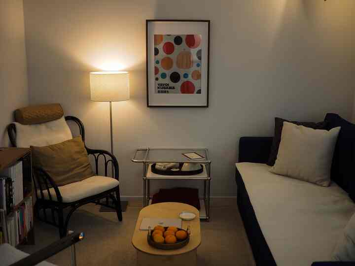 Beige-tone compact living room featuring navy sofa, rattan armchair, floor lamp, and framed poster creating cozy atmosphere