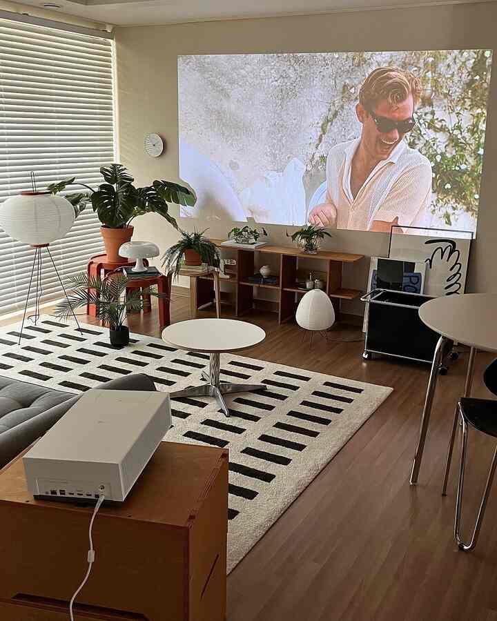 Modern natural living room in white and brown wood tones featuring LG CineBeam projector, wood furniture, and plants