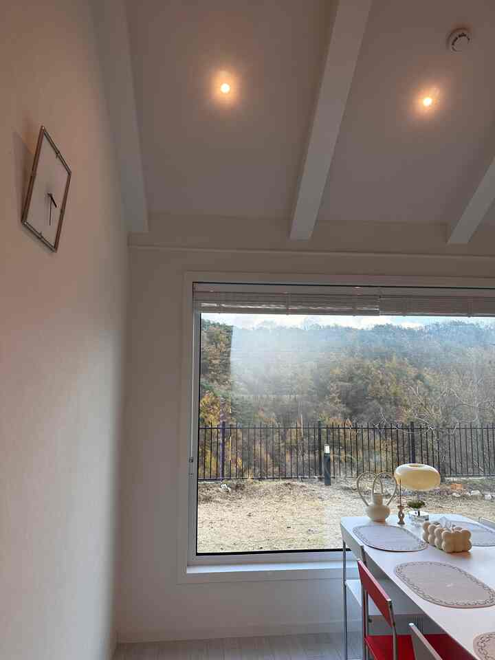 白を基調としたダイニングルーム、大きな窓とシンプルなダイニングテーブル、赤い椅子が配置されたモダンで清潔感のある空間