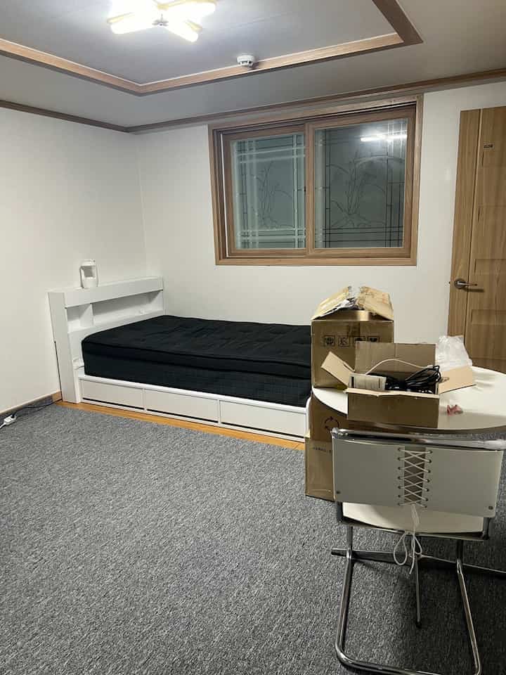 White-toned small single-bedroom with a black mattress bed and a small table arranged in a simple layout