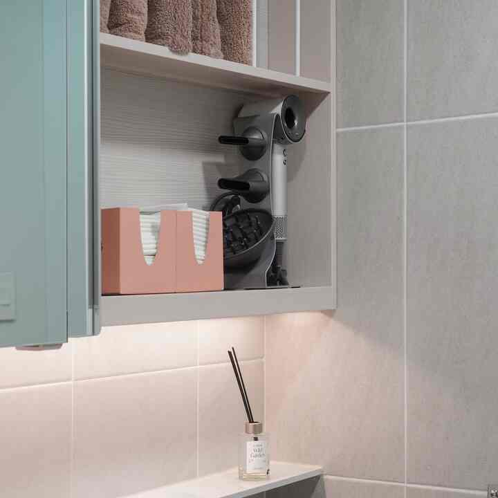 ベージュタイルの壁と木目調の収納棚が調和するバスルーム、ダイソンドライヤースタンドとディフューザーが配置されたミニマルな空間