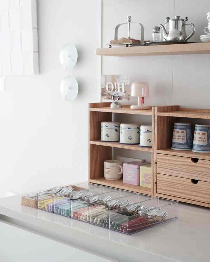White-walled kitchen space with wood tone shelves, featuring colorful cutlery neatly organized in transparent storage containers