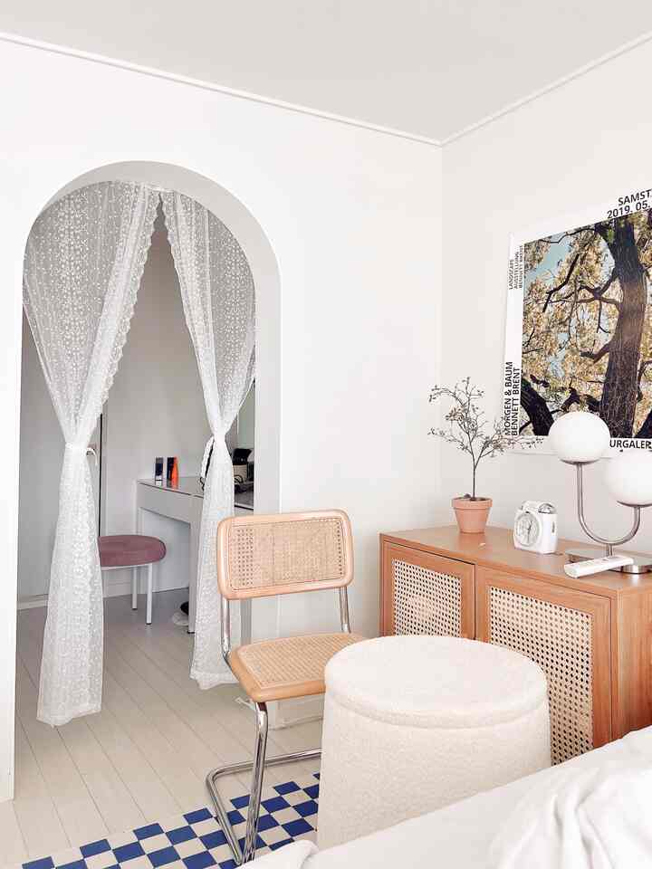Bright white and natural wood-tone bedroom featuring lace curtains and rattan chair creating a cozy and stylish atmosphere