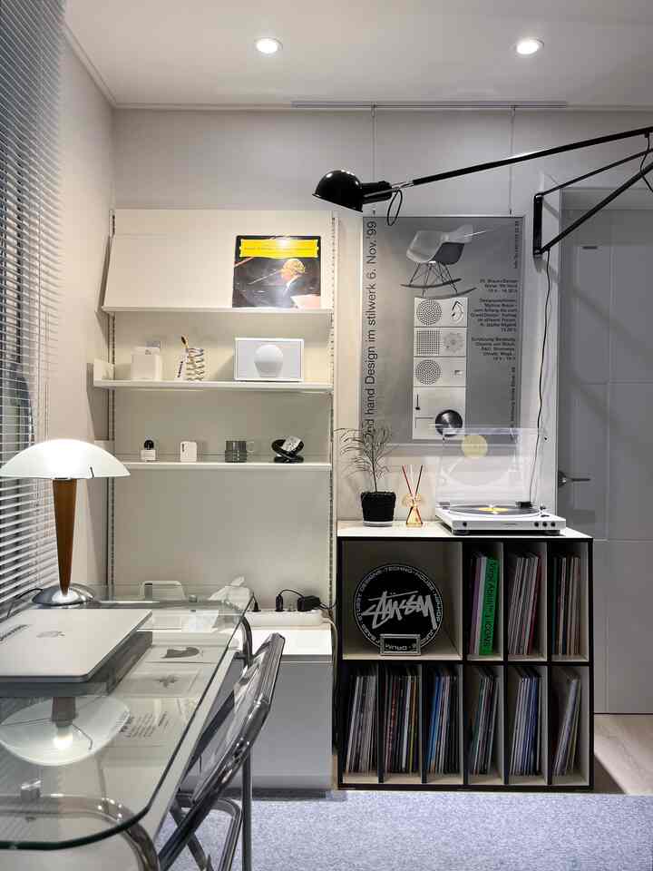 White and gray toned home office space featuring a turntable, vinyl storage cabinet, and lighting, creating a modern and clean music listening area