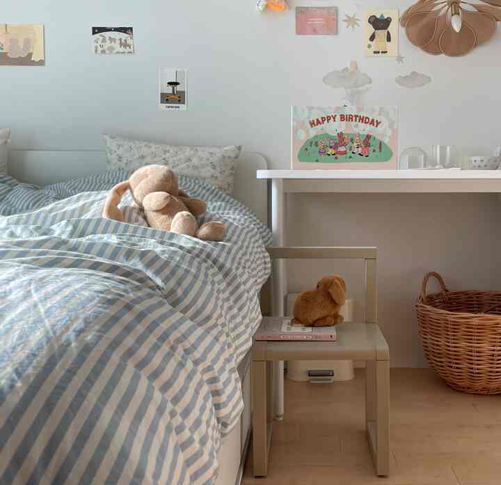 Cozy kids' bedroom with pastel blue striped bedding, beige architect chair, and plush rabbit toys arranged neatly