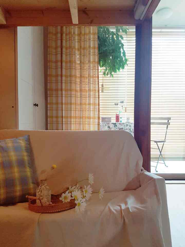 Beige and yellow toned living room featuring checkered curtains and cushions with a rattan tray on sofa creating cozy atmosphere