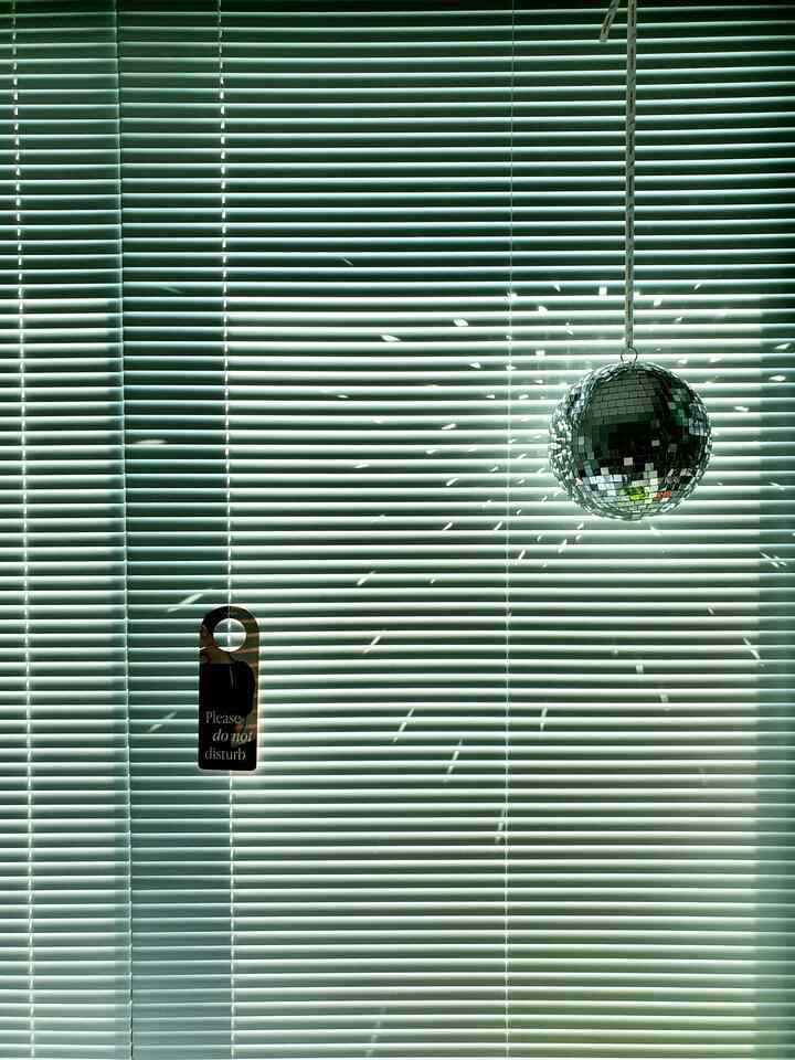 Modern interior featuring silver mirror ball hanging in front of window blinds with striking light reflections