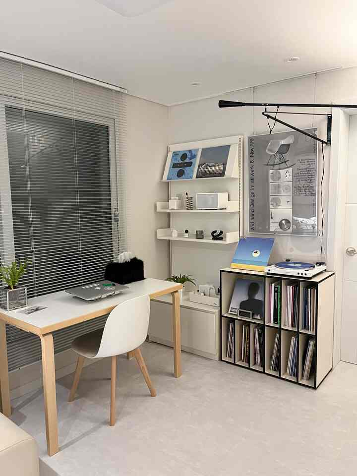 A white and wood tone home office with wall shelves and a vinyl storage unit creating a clean music listening space