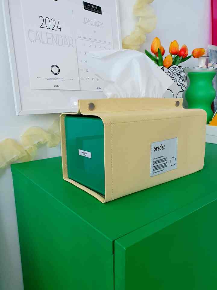 A cozy living room featuring a bright lemon yellow tissue case on a green cabinet, calendar posters on the wall, and a vase with tulips.