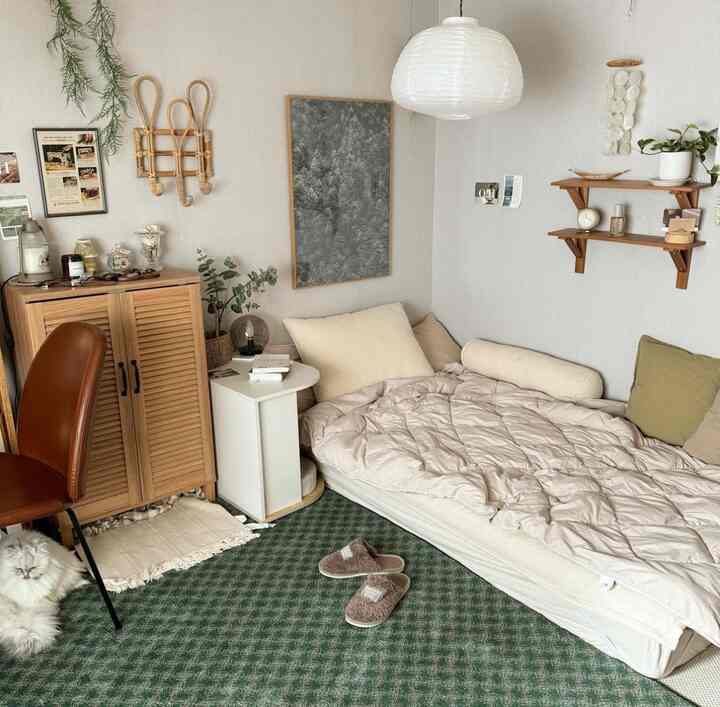 Beige and green toned studio bedroom featuring floor mattress, rattan decor, and plants with a natural atmosphere