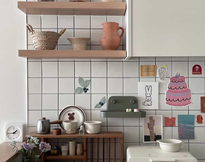 White tiled wall kitchen space with wood-toned shelves featuring small kitchen items and a clock, creating a tidy atmosphere