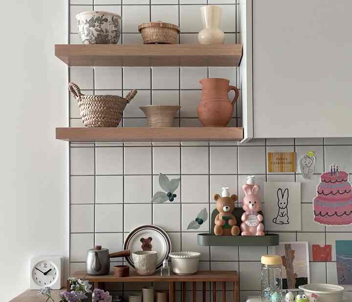 ナチュラルカラーの木製棚と白いタイル壁のキッチン、かわいい装飾と皿が配置された落ち着いた雰囲気のインテリア