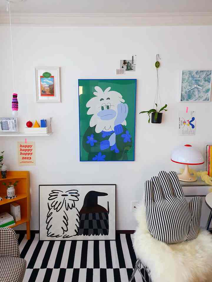 白い壁とモノトーンのストライプラグがあるリビング、カラフルなポスターと額縁アートが配置された印象的な空間