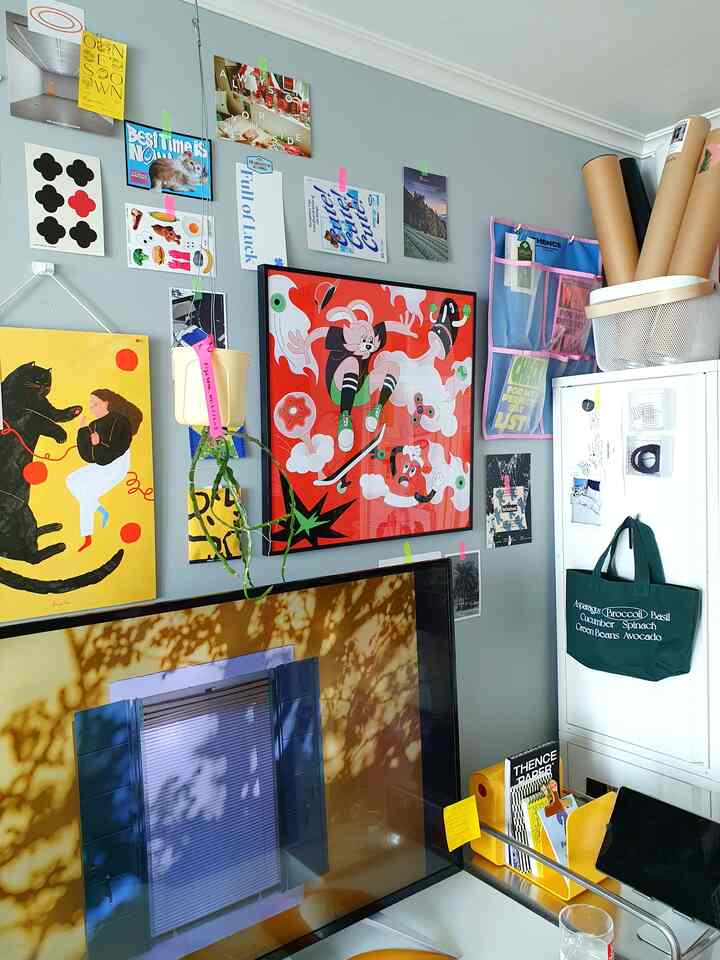 明るくカラフルなポスターと額縁が飾られたパステルブルーの壁、白い家具が配された落ち着いたホームオフィス