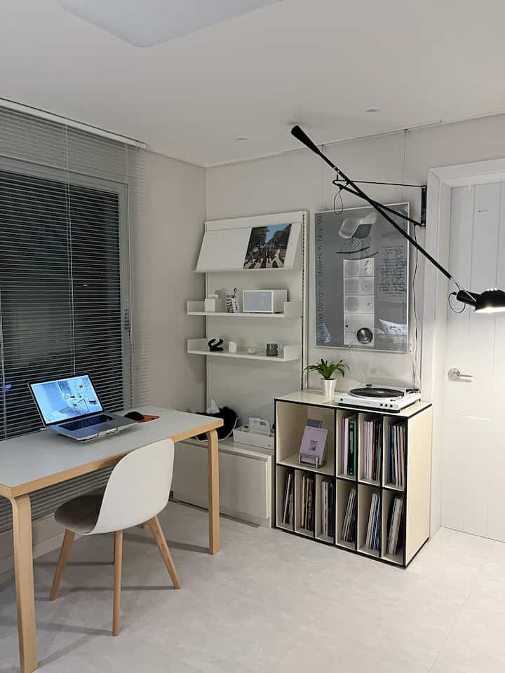 White and wood-toned home office featuring a compact desk, storage units, and a turntable, creating a minimal and quiet atmosphere