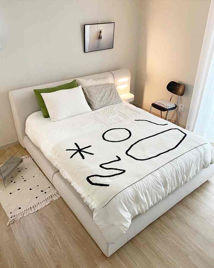 Ivory-toned bedroom featuring a soft rounded bed frame, various cushions, and natural wood flooring creating a cozy atmosphere