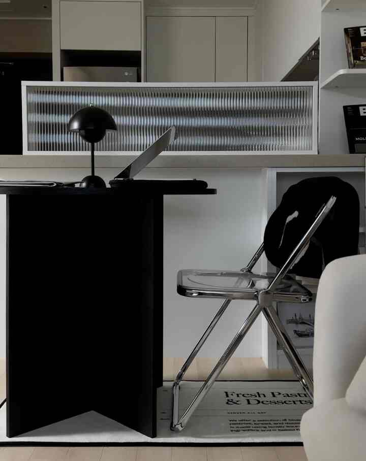 モノトーンのリビングルーム、キッチンを仕切るアイランド間仕切り、黒いテーブルと透明な折りたたみ椅子が配置されたミニマルなインテリア