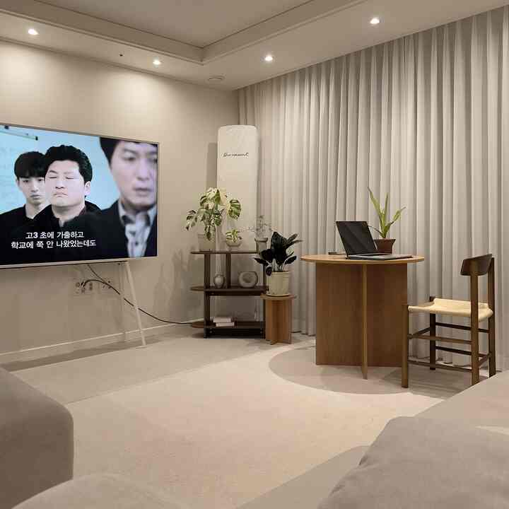 白を基調としたナチュラルモダンなリビングルーム、茶色の木製丸テーブルと椅子、植物、テレビが配置された雰囲気のあるインテリア