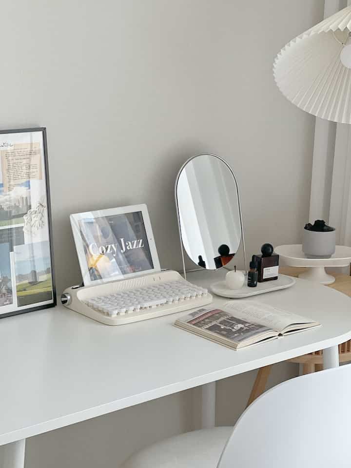 White-toned bedroom study featuring a half-oval desk with retro keyboard, iPad, and mirror in a clean simple atmosphere