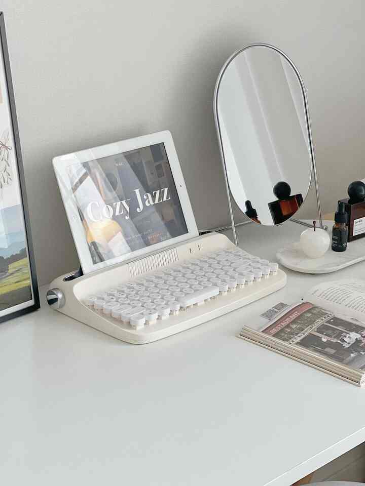 White-toned desk featuring a retro keyboard, mirror, and diffuser creating a simple home office space