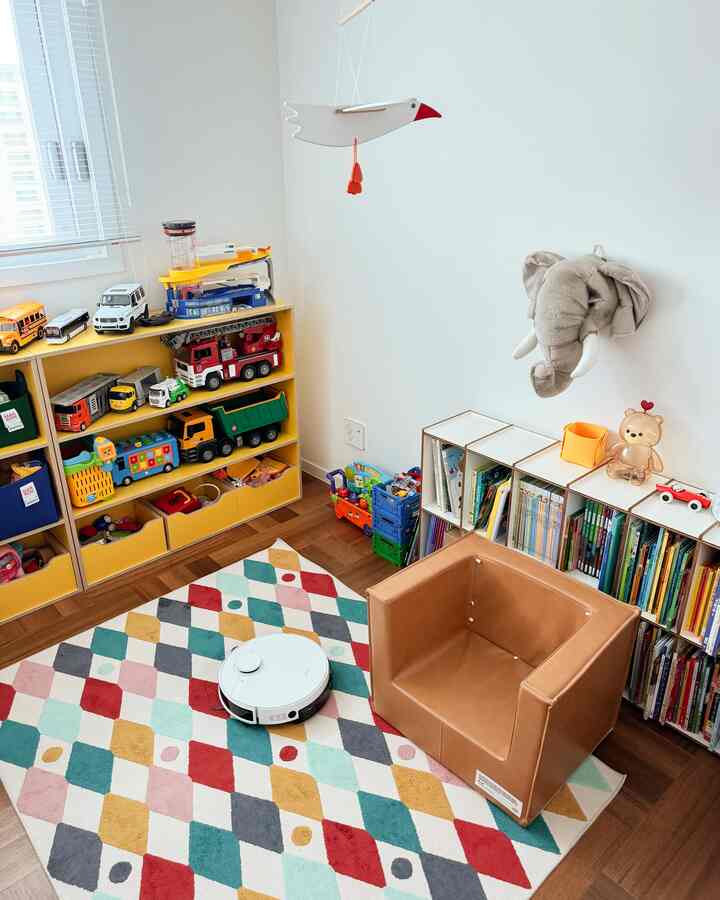 明るい黄色のおもちゃ棚とカラフルなラグがある子供部屋、ナチュラルなブラウンの床と落ち着いた雰囲気のインテリア