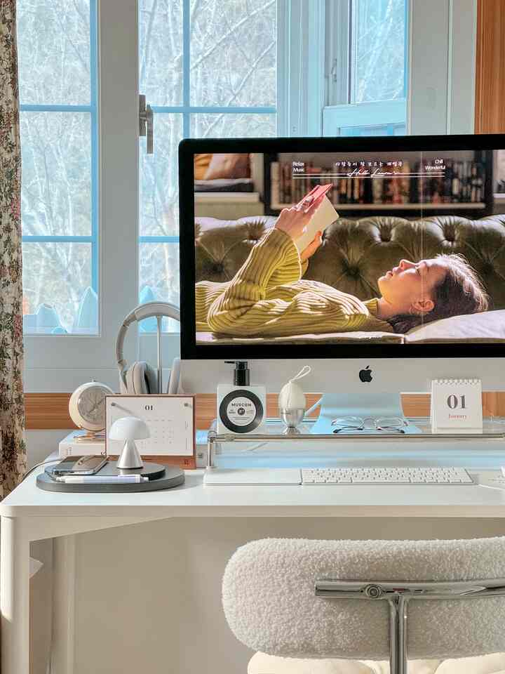 Bright white-toned home office space featuring a clean desk with monitor stand and two calendars, organized workspace