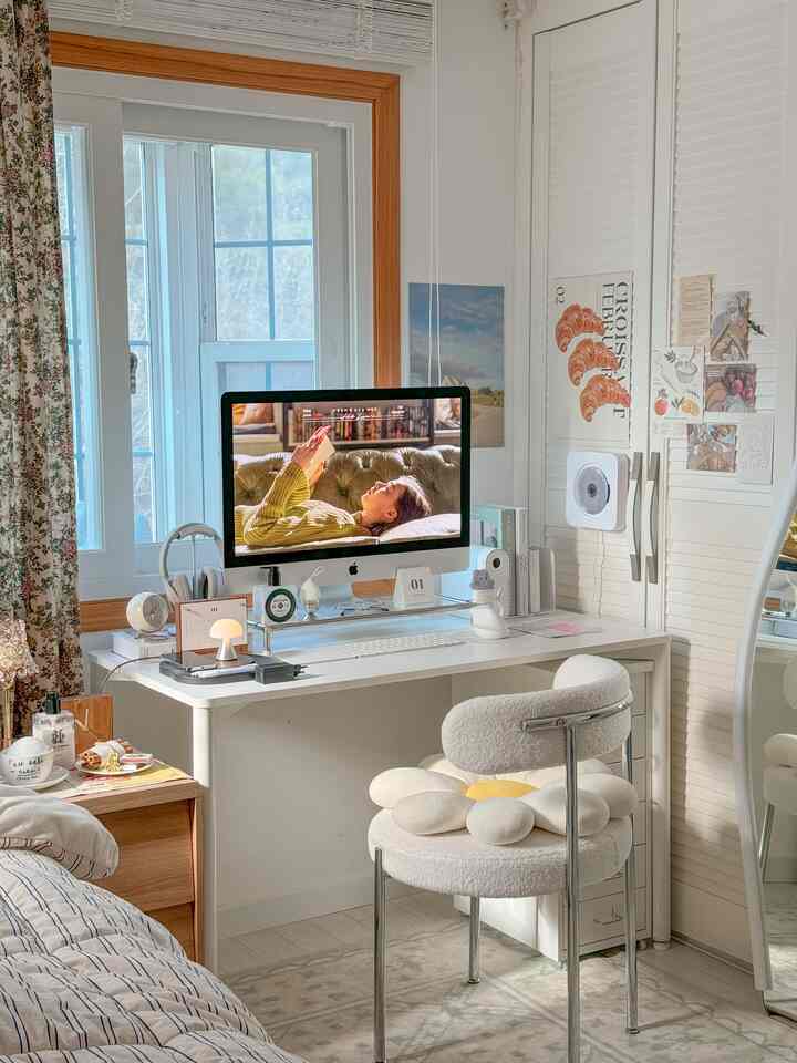 White and wood tone home office space featuring a large computer screen and cozy desk accessories, creating a warm and inviting workspace
