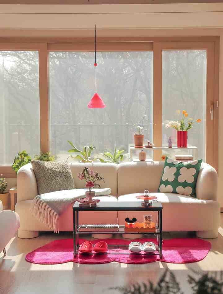Bright beige sofa and pink rug in living room featuring coffee table and various plants with a modern atmosphere