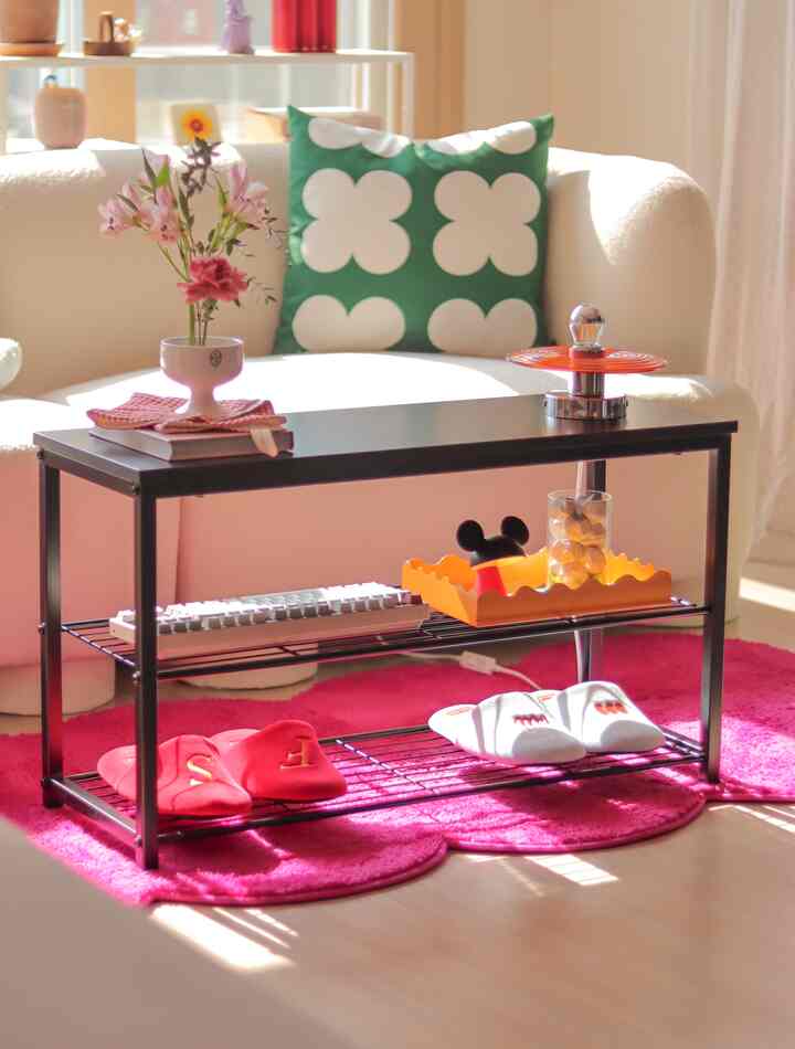 A bright living room with white sofa featuring green cushions, a black coffee table, and slippers on a pink rug